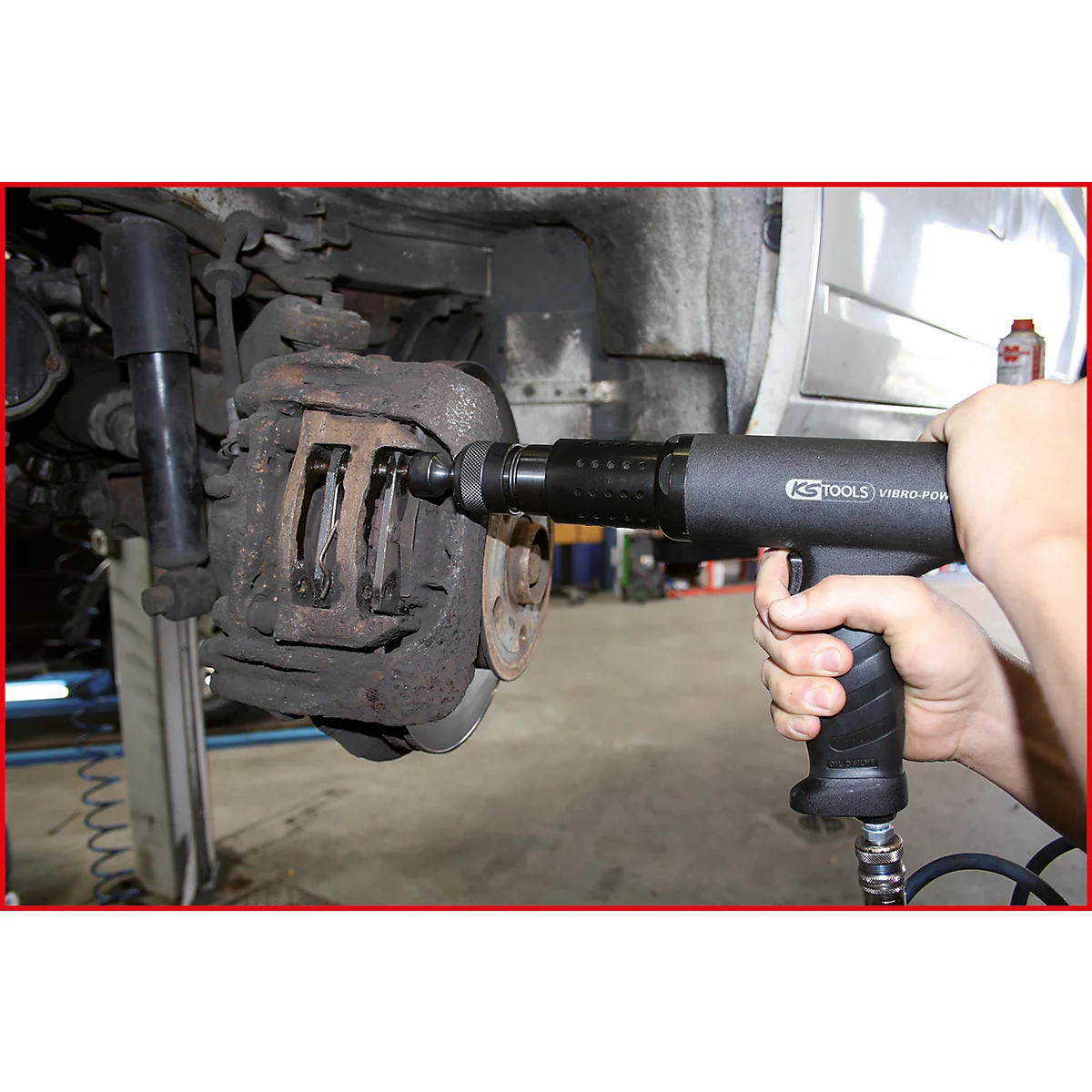 Nahaufnahme einer Bremse, die mit einem Druckluftwerkzeug bearbeitet wird. Das Werkzeug, KS TOOLS, wird von einer Hand gehalten.